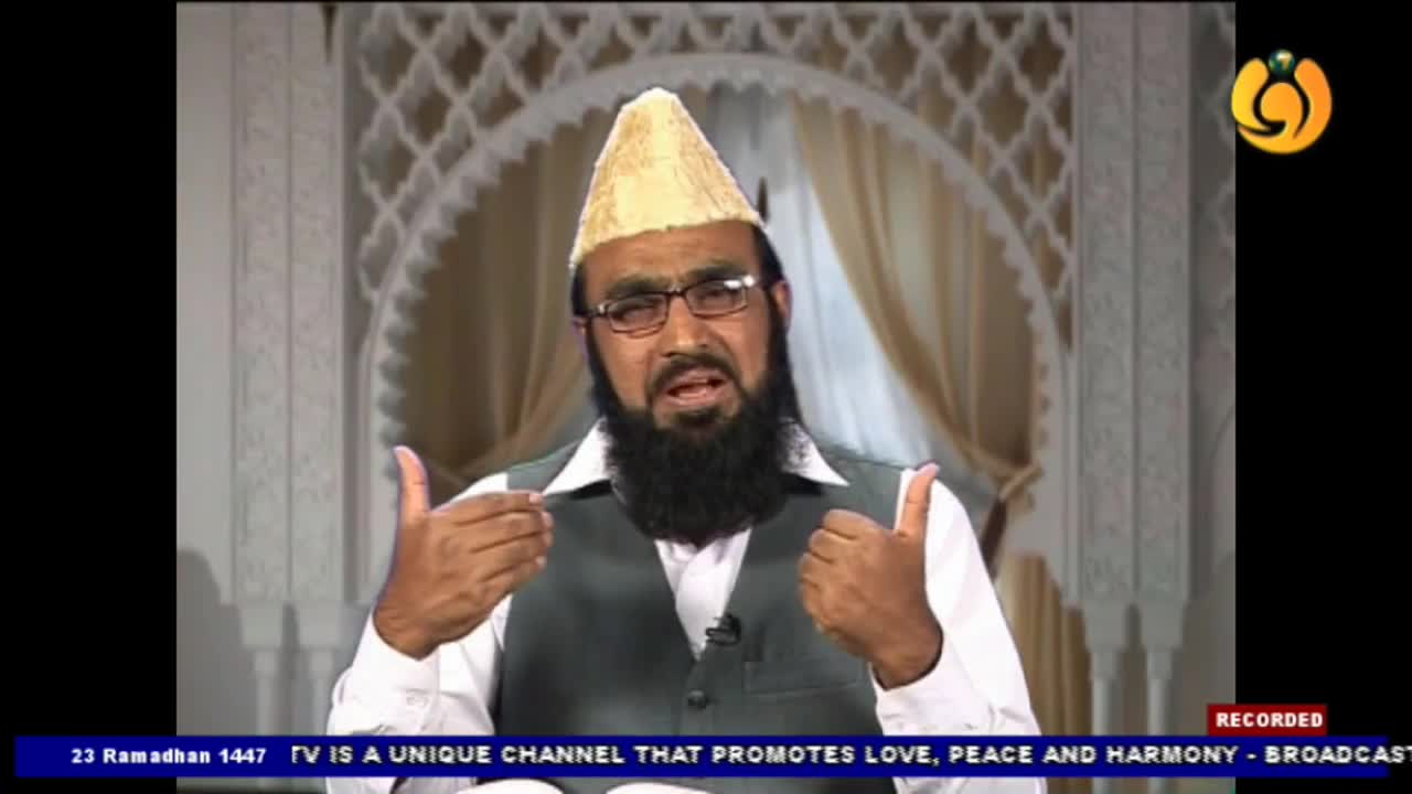 A man with a beard and glasses gestures with his hands as he speaks. He wears a light-colored cap and a dark vest over a white shirt, his words broadcast on Noor TV.