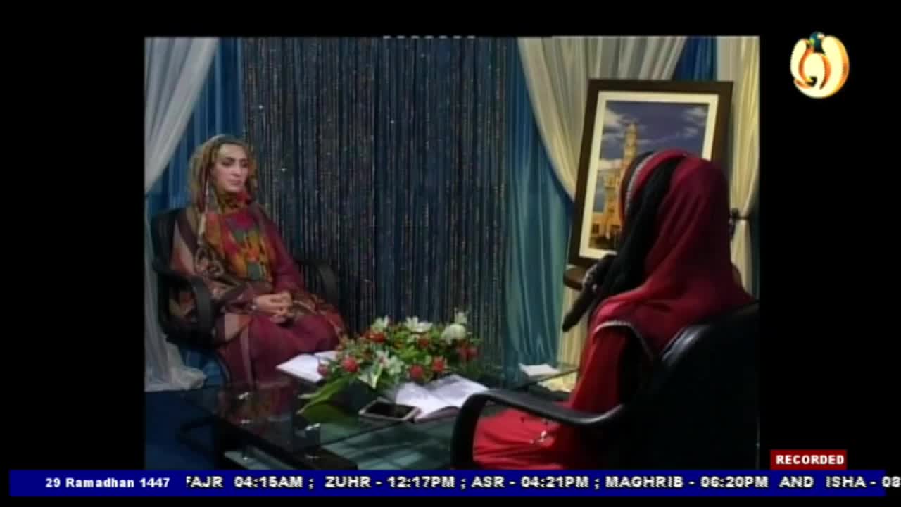 A woman in a colourful hijab and maroon dress sits on the left, facing forward. To her right, another woman, also in a red hijab, speaks into a microphone, her back to the camera. A woman in a colourful hijab and maroon dress sits on the left, facing forward. To her right, another woman, also in a red hijab, speaks into a microphone, her back to the camera.