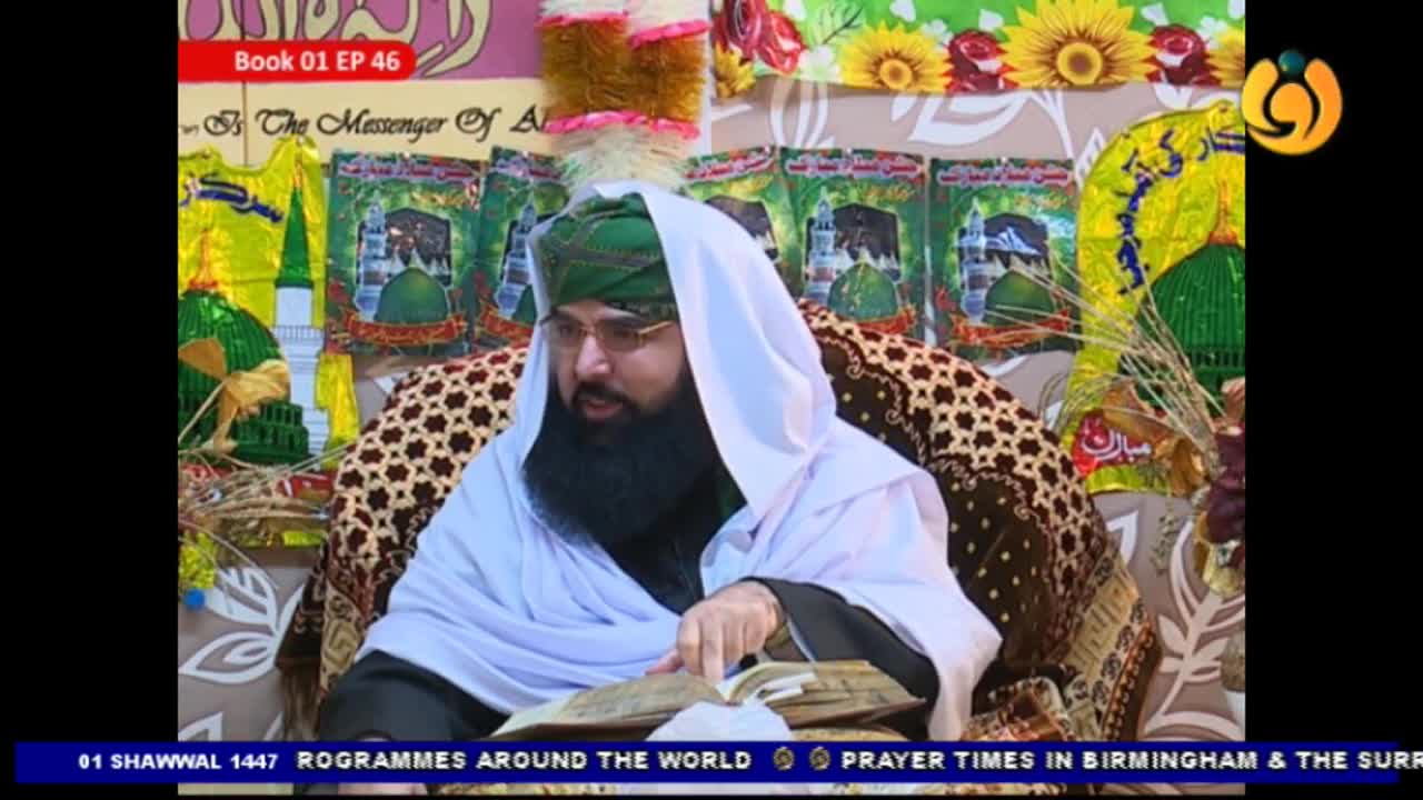 A man wearing a green turban and white shawl sits, engrossed in a book. Behind him, colorful banners display images of mosques and Arabic script, typical of Noor TV broadcasts from the UK. A man wearing a green turban and white shawl sits, engrossed in a book. Behind him, colorful banners display images of mosques and Arabic script, typical of Noor TV broadcasts from the UK.