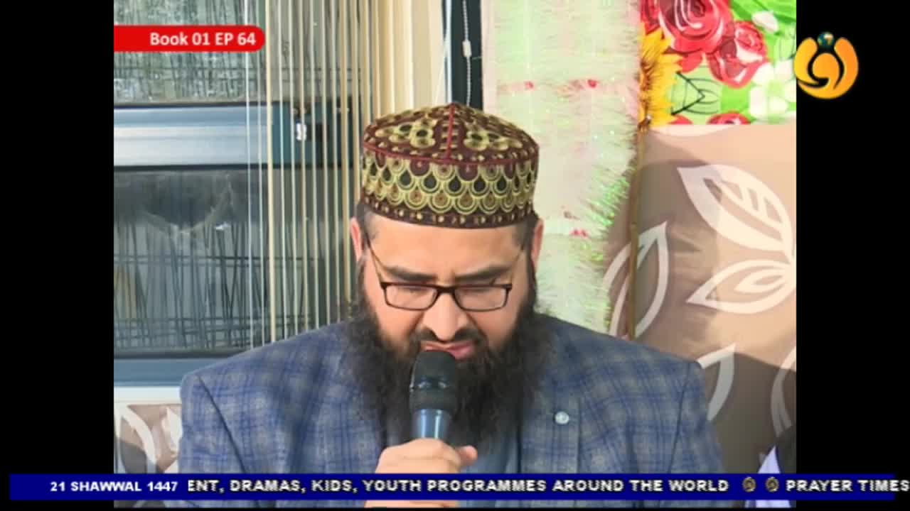 A man with a beard and glasses, wearing a patterned cap, speaks into a microphone. He's dressed in a checkered jacket, and behind him, a backdrop features floral patterns and decorative lights. A man with a beard and glasses, wearing a patterned cap, speaks into a microphone. He's dressed in a checkered jacket, and behind him, a backdrop features floral patterns and decorative lights.
