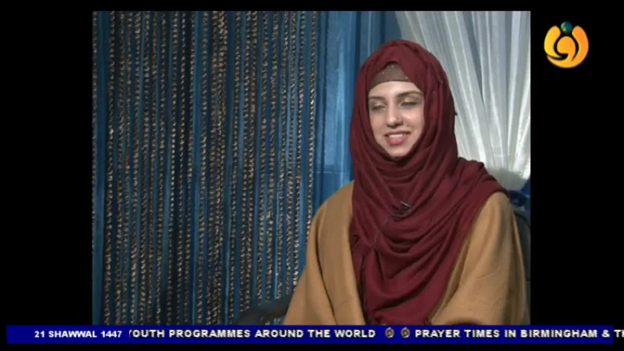A young woman in a maroon hijab and tan coat smiles, her gaze directed slightly off-camera. Behind her, strands of beaded curtains hang in vertical lines. A young woman in a maroon hijab and tan coat smiles, her gaze directed slightly off-camera. Behind her, strands of beaded curtains hang in vertical lines.