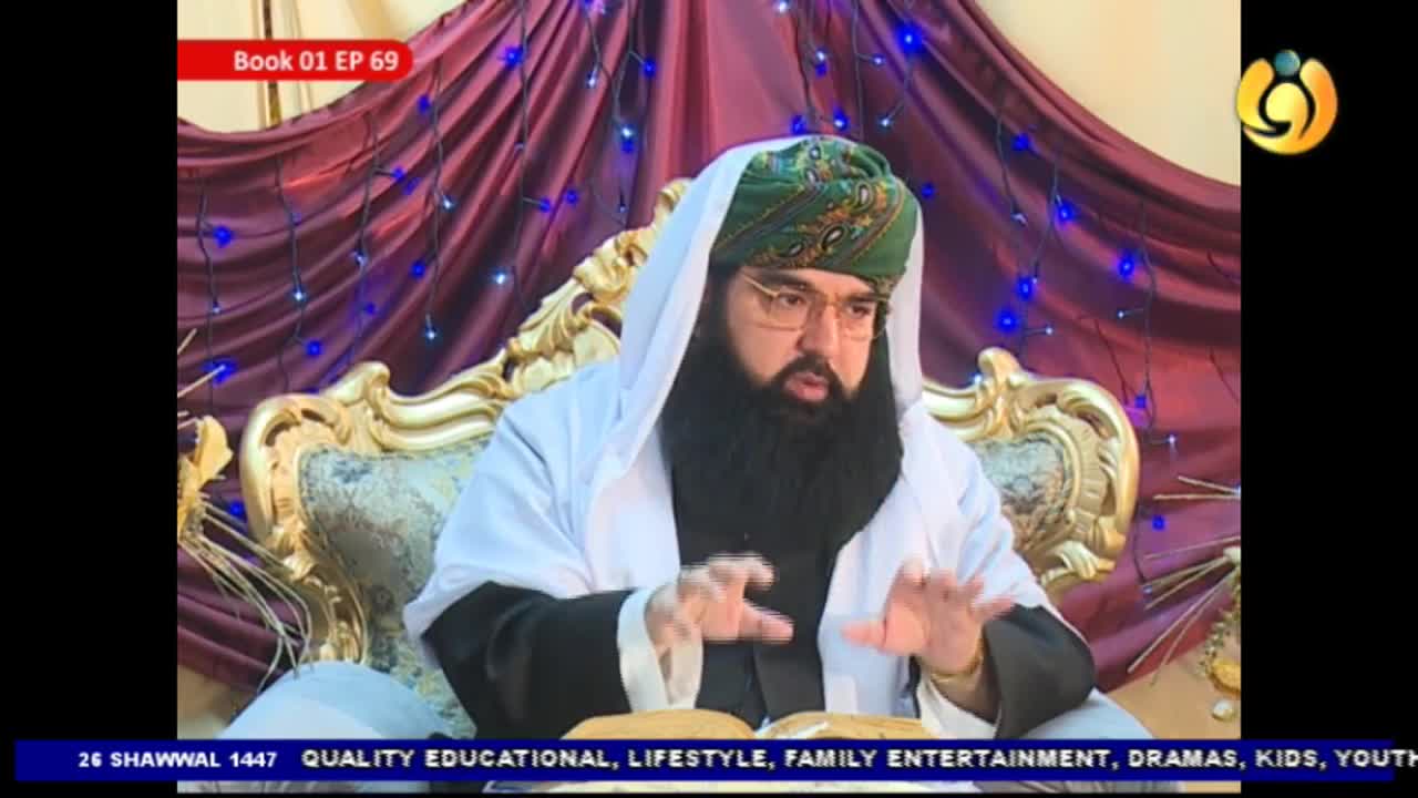 A man in a green turban and white robe gestures with his hands while speaking. He sits on a golden chair in front of a burgundy curtain with blue lights.