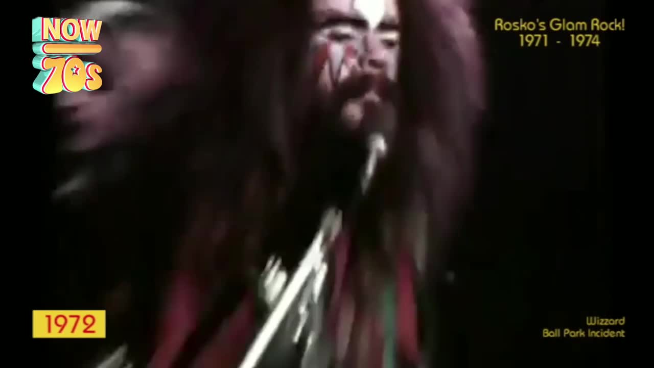 The singer, face painted, is leaning into the microphone, his hair a wild explosion. The stage lights catch the silver of his guitar as he strums.
