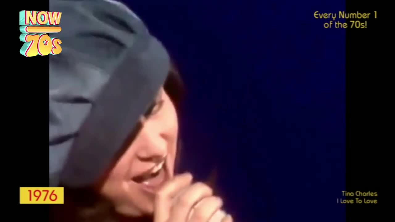 The singer, wearing a dark hat, is mid-song, her mouth open as she belts out the tune. The stage is dark, but the bright "Now 70s" logo and the year 1976 on the screen give the context.
