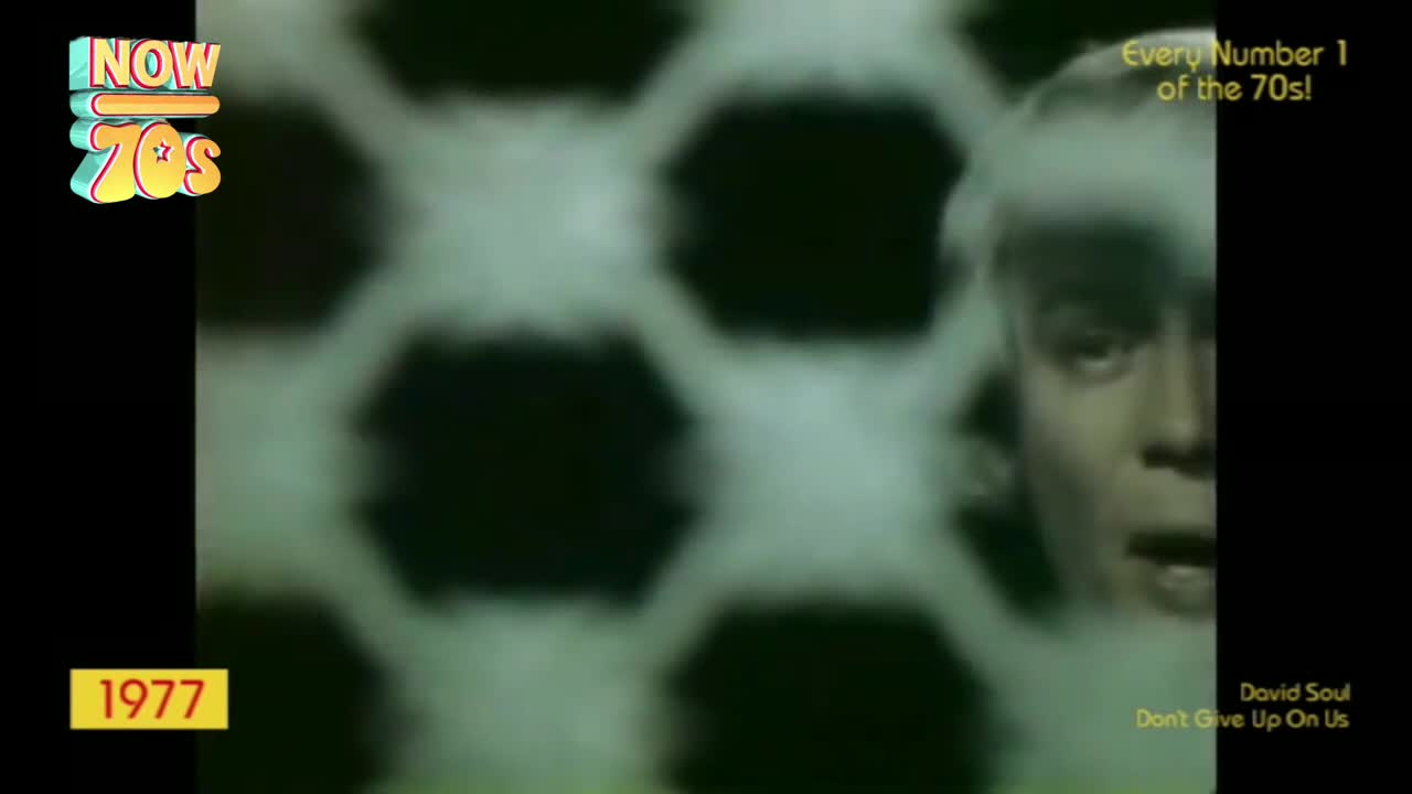 A man with pale hair is singing, his face partially obscured by a blurry, honeycomb-like pattern. The year 1977 is displayed, alongside the title of a song by David Soul.
