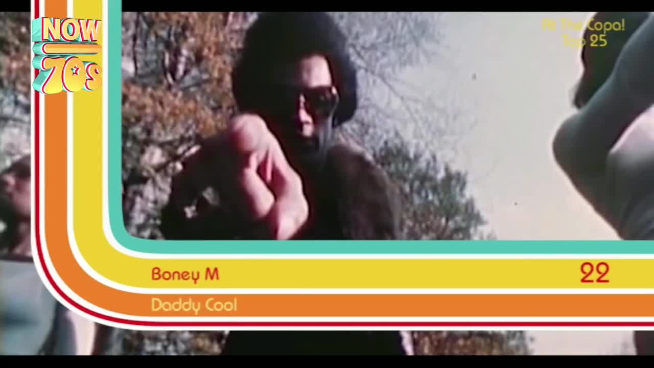 A man in sunglasses and a big afro points directly at the camera. Behind him, the trees are a bit out of focus.
