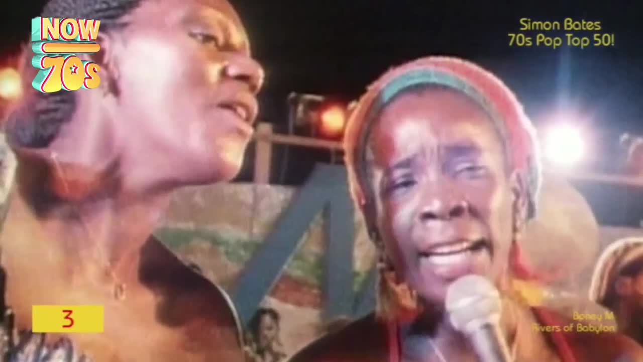 A woman with a microphone sings, her face illuminated by stage lights. Beside her, another singer looks on, their voices blending into the song.
