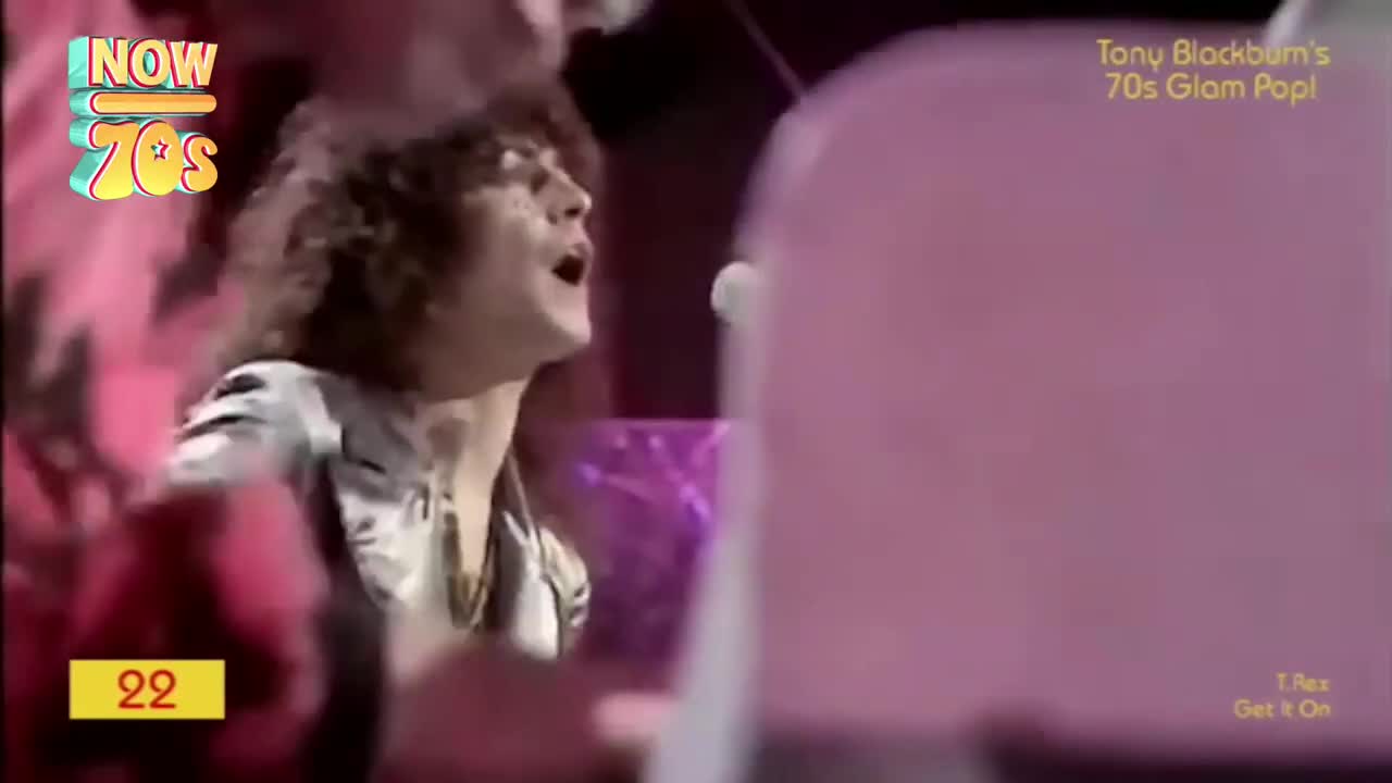 The singer, hair a mass of curls, throws his head back, belting into the microphone. A flash of silver fabric on his shirt catches the light as he moves.
