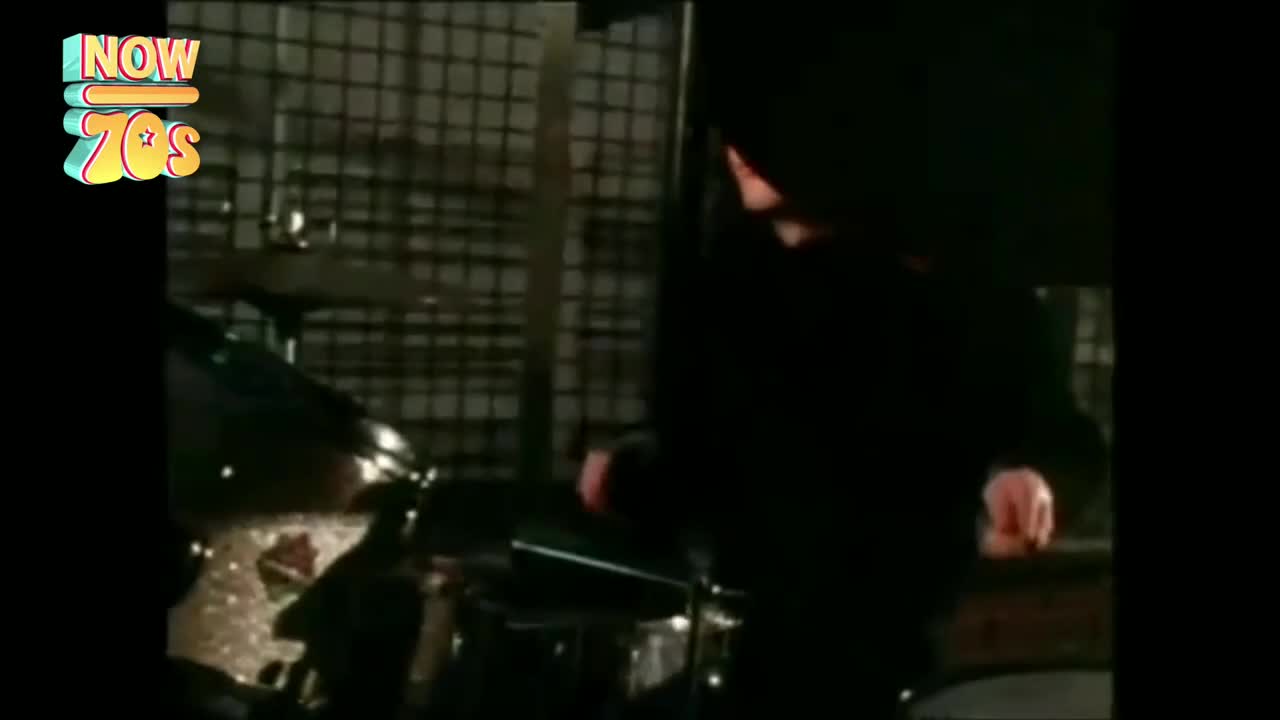 The drummer's arms are a blur, hitting the snare and cymbals with force. It's a tight, dark stage, but the energy is electric.
