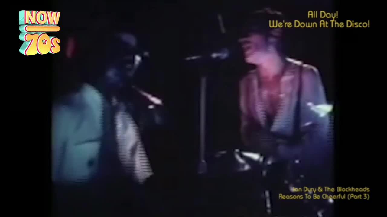 The singer, bathed in stage light, leans into the microphone, his shirt open. Beside him, a figure in a hat holds a saxophone, ready to play.
The singer, bathed in stage light, leans into the microphone, his shirt open. Beside him, a figure in a hat holds a saxophone, ready to play.