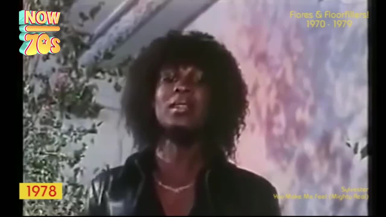 A singer with a big, curly afro is singing, his lips moving as he belts out a tune. Behind him, a painted backdrop with soft, pastel colors provides a hazy background.
A singer with a big, curly afro is singing, his lips moving as he belts out a tune. Behind him, a painted backdrop with soft, pastel colors provides a hazy background.