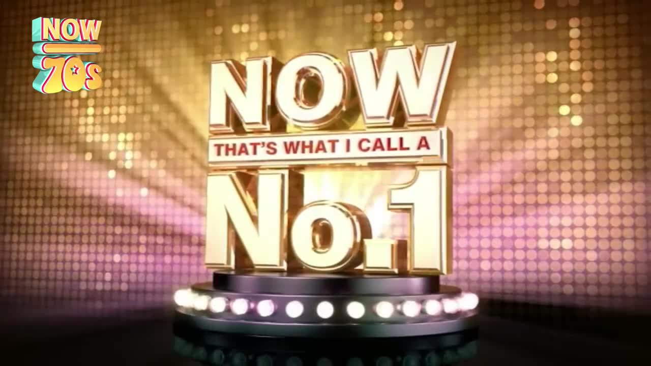 A golden "NOW" logo, with "THAT'S WHAT I CALL A No.1" underneath, sits on a stage lit by small bulbs. The background shimmers with a dotted pattern of gold and pink.
A golden "NOW" logo, with "THAT'S WHAT I CALL A No.1" underneath, sits on a stage lit by small bulbs. The background shimmers with a dotted pattern of gold and pink.