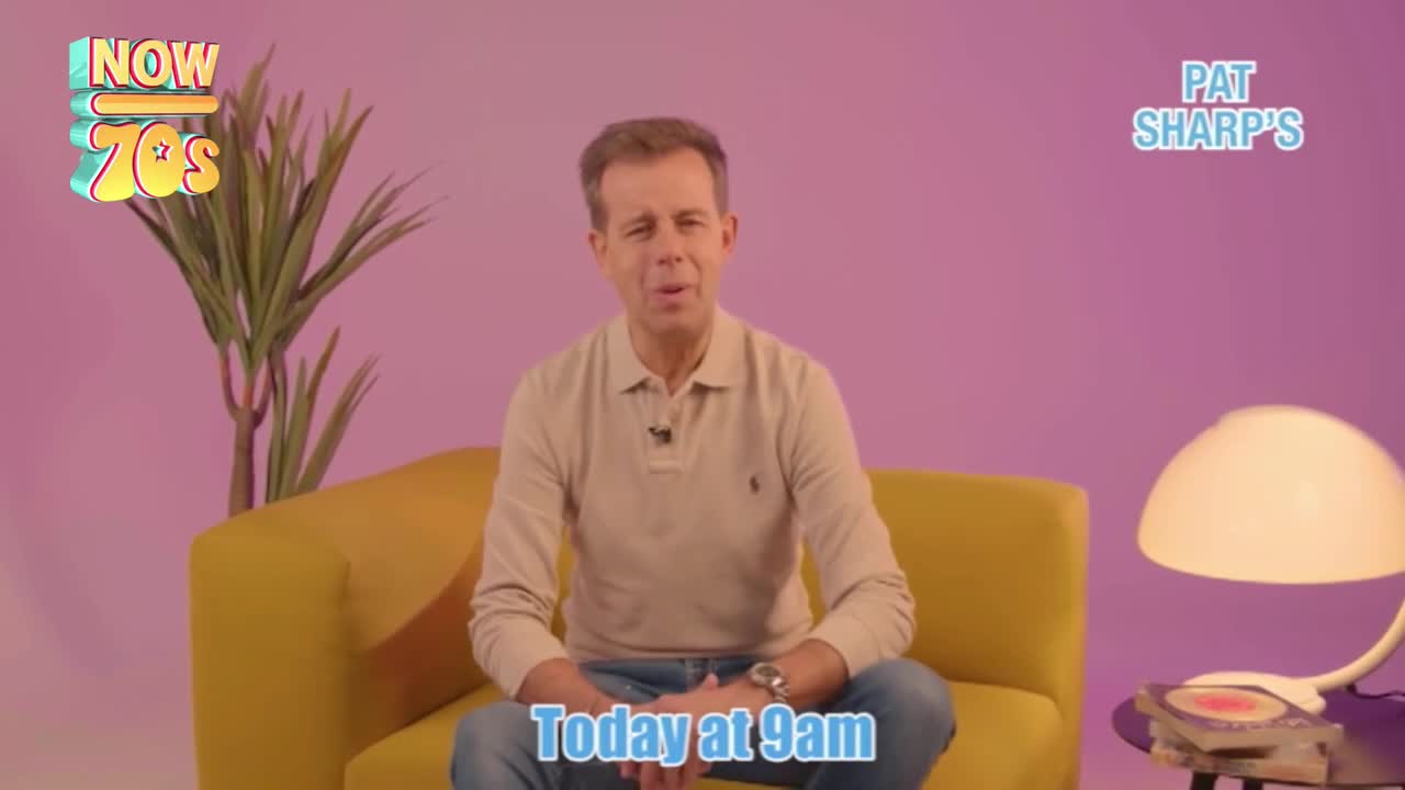 He's sitting on a yellow sofa, speaking into a small microphone. The background is a soft purple, and a retro-style lamp sits beside him.
He's sitting on a yellow sofa, speaking into a small microphone. The background is a soft purple, and a retro-style lamp sits beside him.
