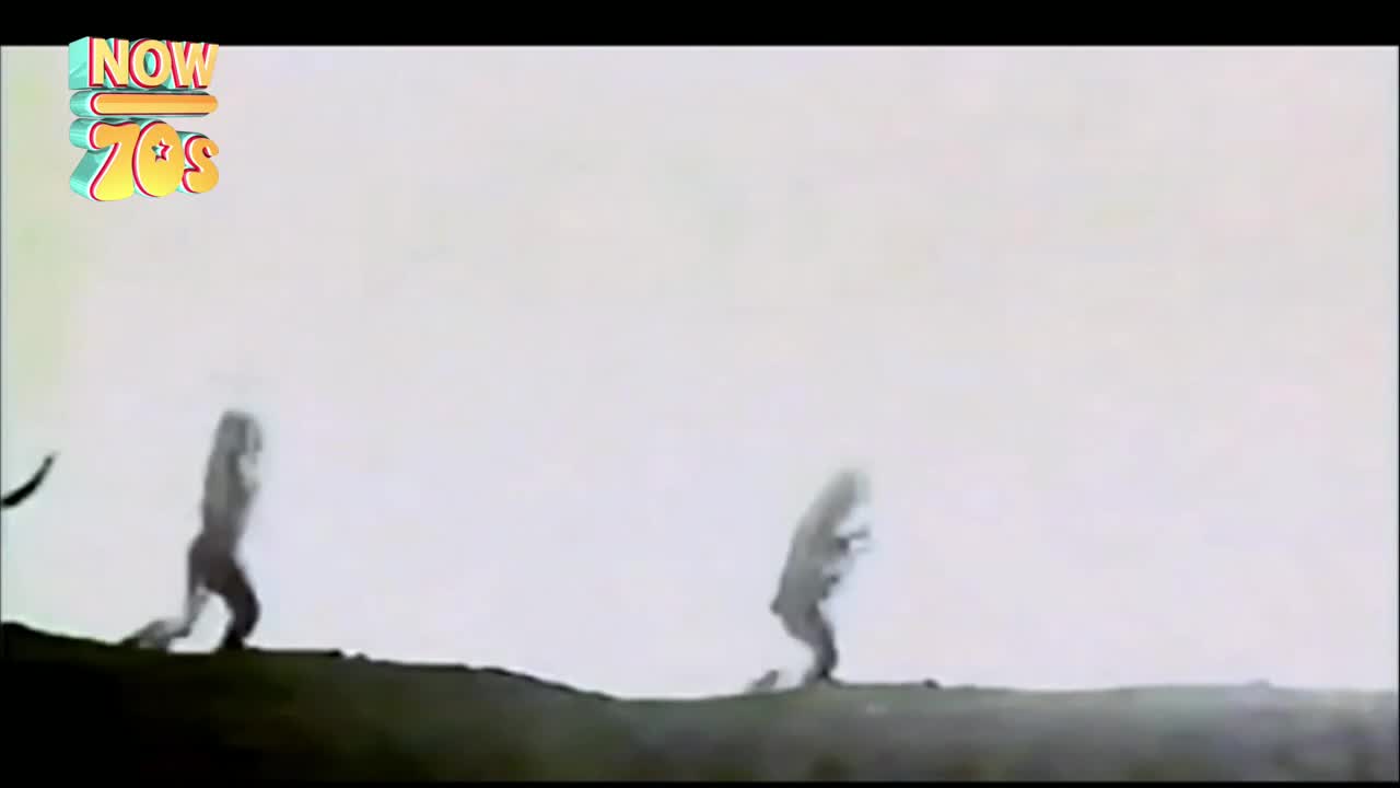 Two figures, blurred by motion, are running across the crest of a hill. They appear to be in silhouette against a bright, overcast sky.

