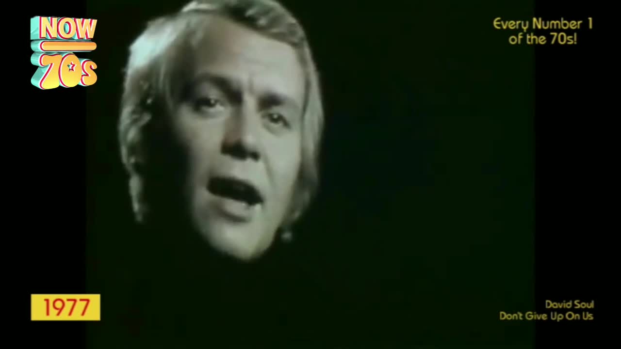 The singer's face, lit from above, fills the screen as he sings. The black background makes him seem to float, his mouth open as he delivers the song.
