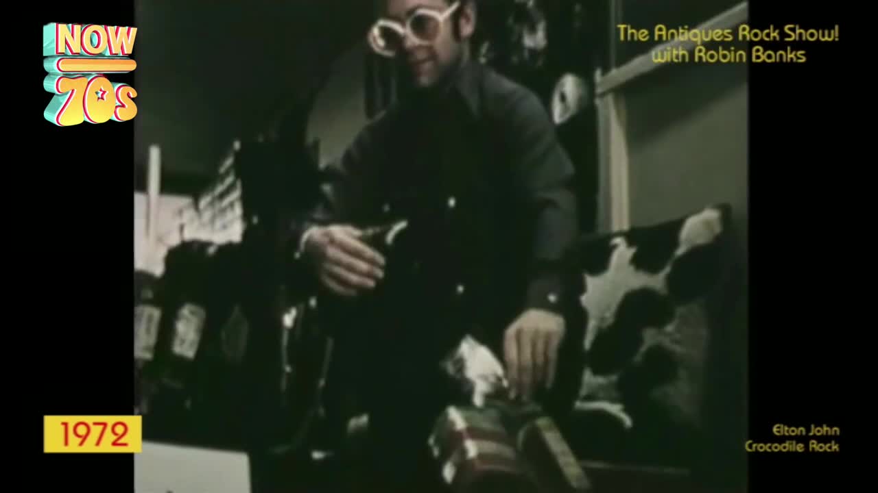Elton John, sporting enormous round glasses, strums a guitar in this 1972 clip. He's on "The Antiques Rock Show!" with Robin Banks.