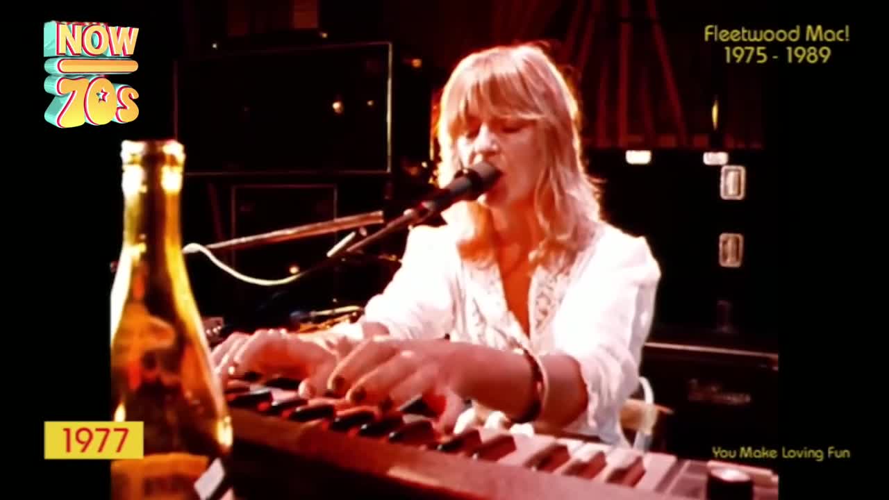 A woman with blonde hair plays a keyboard, her fingers moving across the keys. A bottle of what looks like Harp Lager stands to her left, a subtle nod to the era.