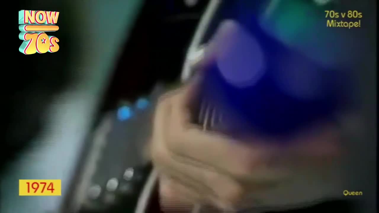 A hand grips a microphone, its blue casing catching the stage lights. The year 1974 flashes on screen, a reminder of the era.