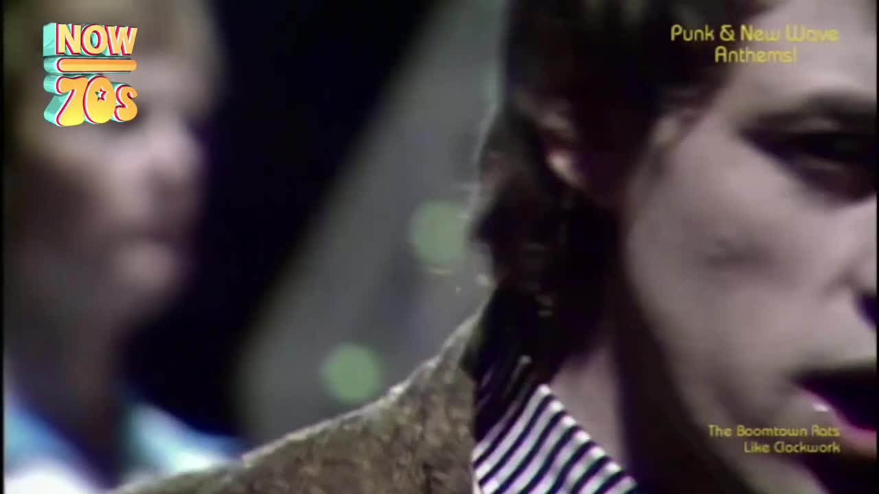 The singer leans into the microphone, his striped shirt collar visible. The Boomtown Rats are playing "Like Clockwork."