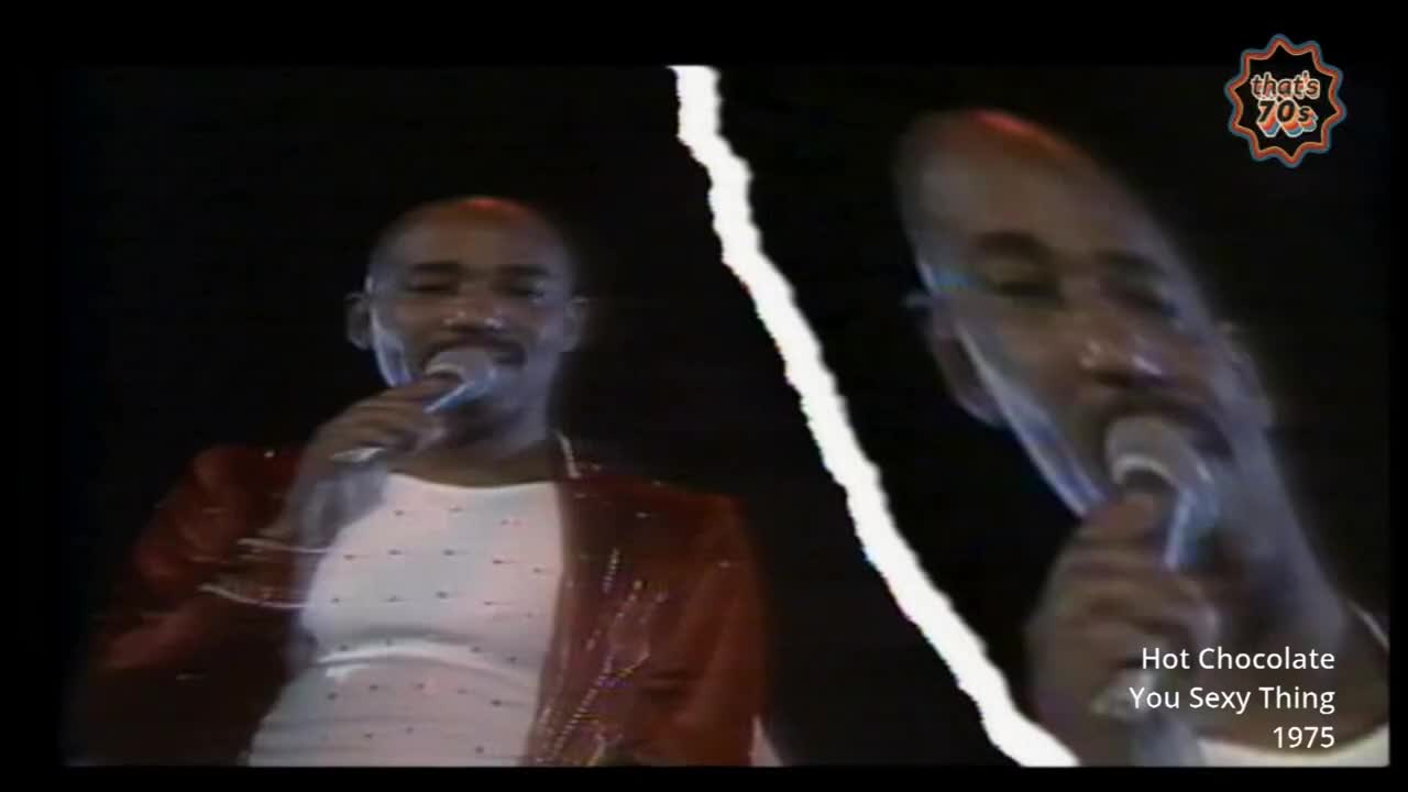 A man in a sparkly red jacket sings into a microphone, his face split down the middle. The other half of his face, distorted, also sings into a microphone.