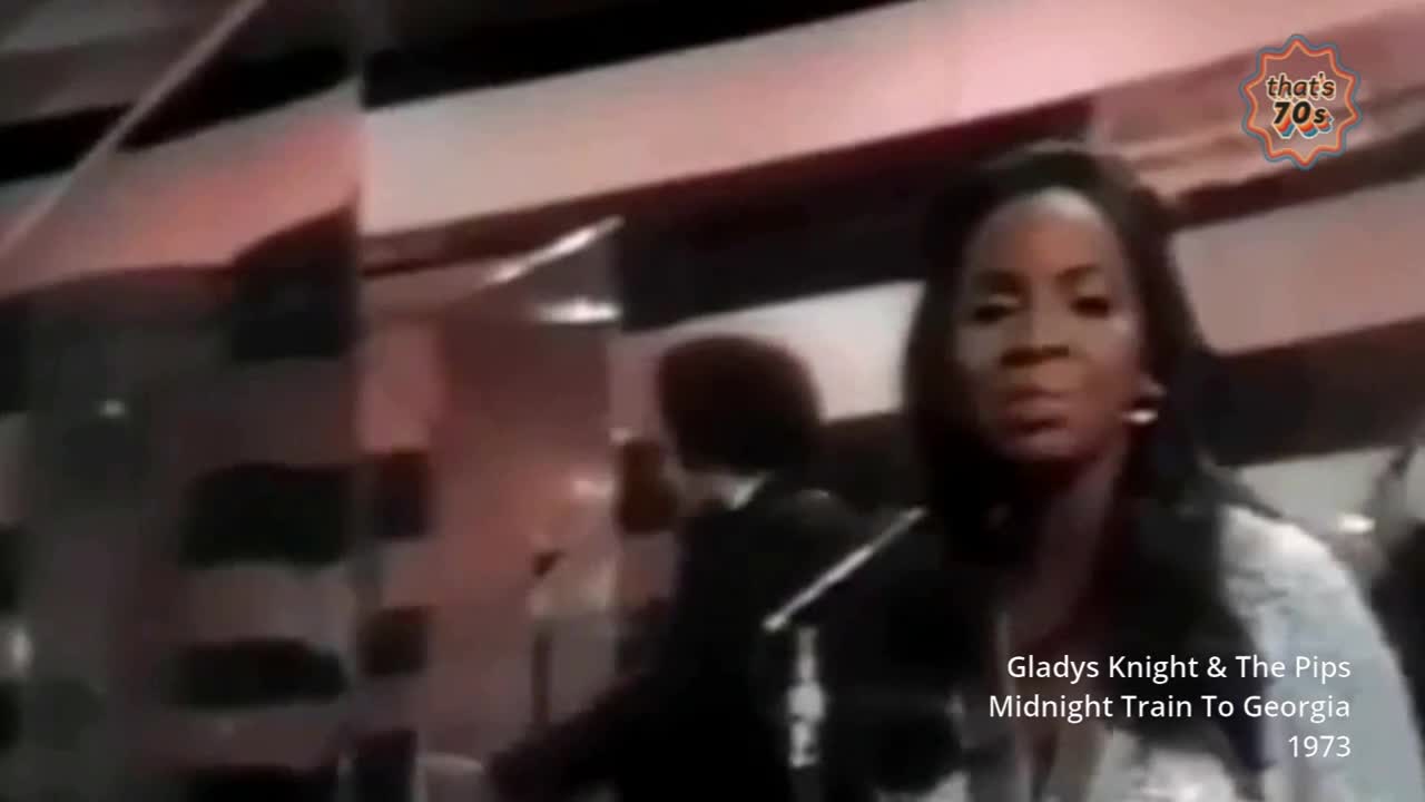 Gladys Knight stands centre stage, her gaze fixed forward as the band behind her plays. The stage lights cast a warm glow on the scene, a familiar sight from a 1970s television performance.
