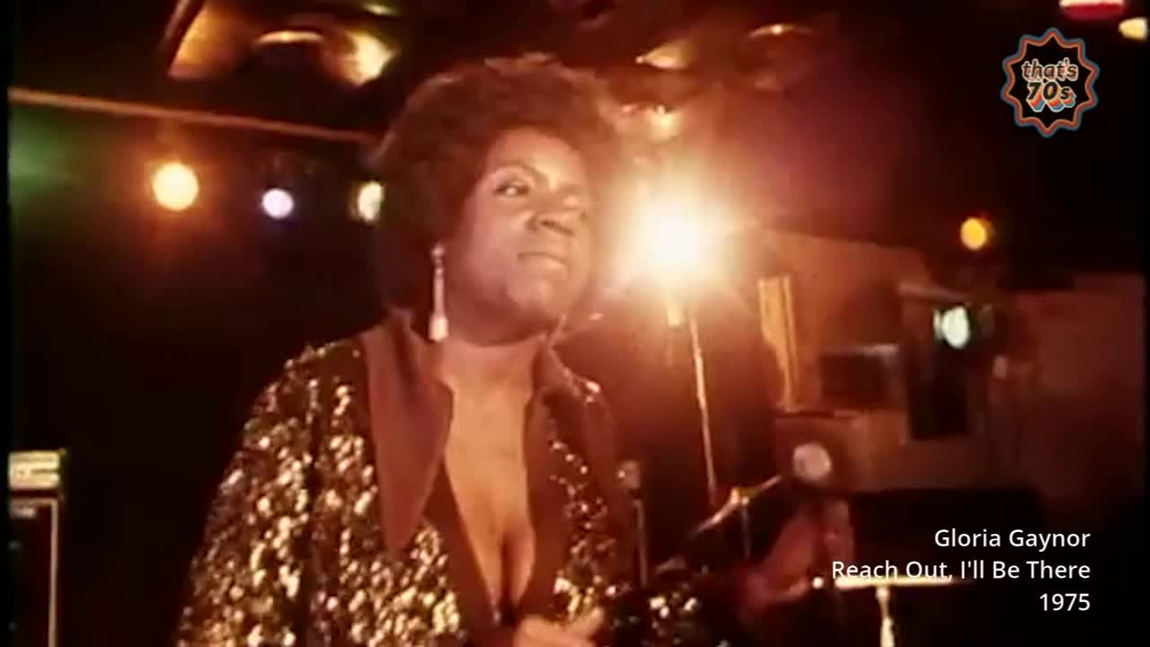 A singer in a sequined jacket belts out a tune under bright stage lights. The crowd is a dark mass beyond the spotlight's reach.