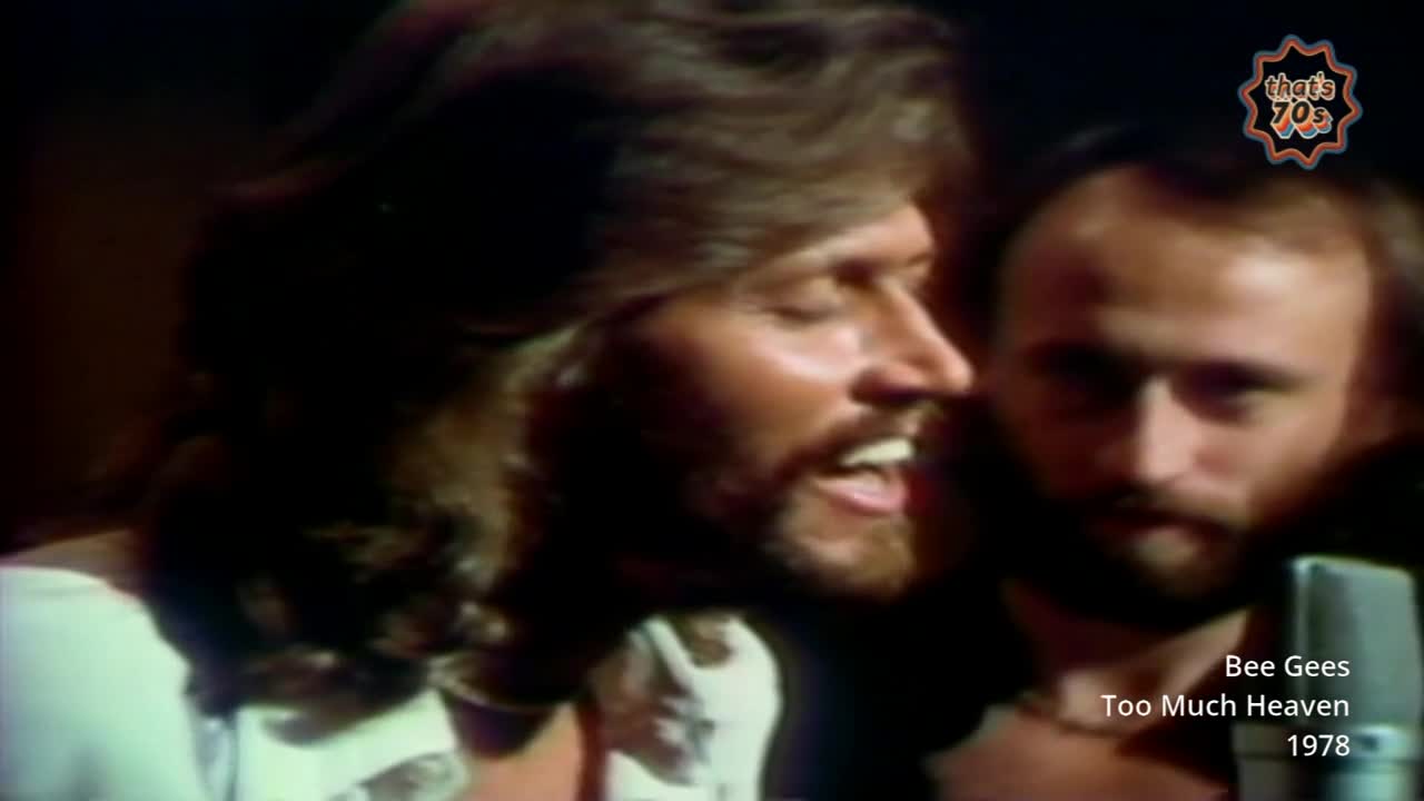 Barry Gibb belts out a tune, his eyes closed in concentration. Beside him, Robin Gibb's face is partially obscured as he leans into the microphone.