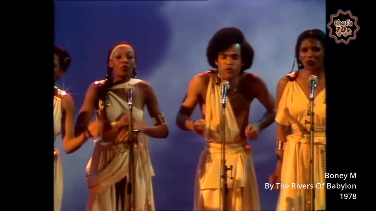 Four singers stand at microphones, their voices filling the air with a powerful sound. They wear flowing white tunics, their movements synchronized as they perform.