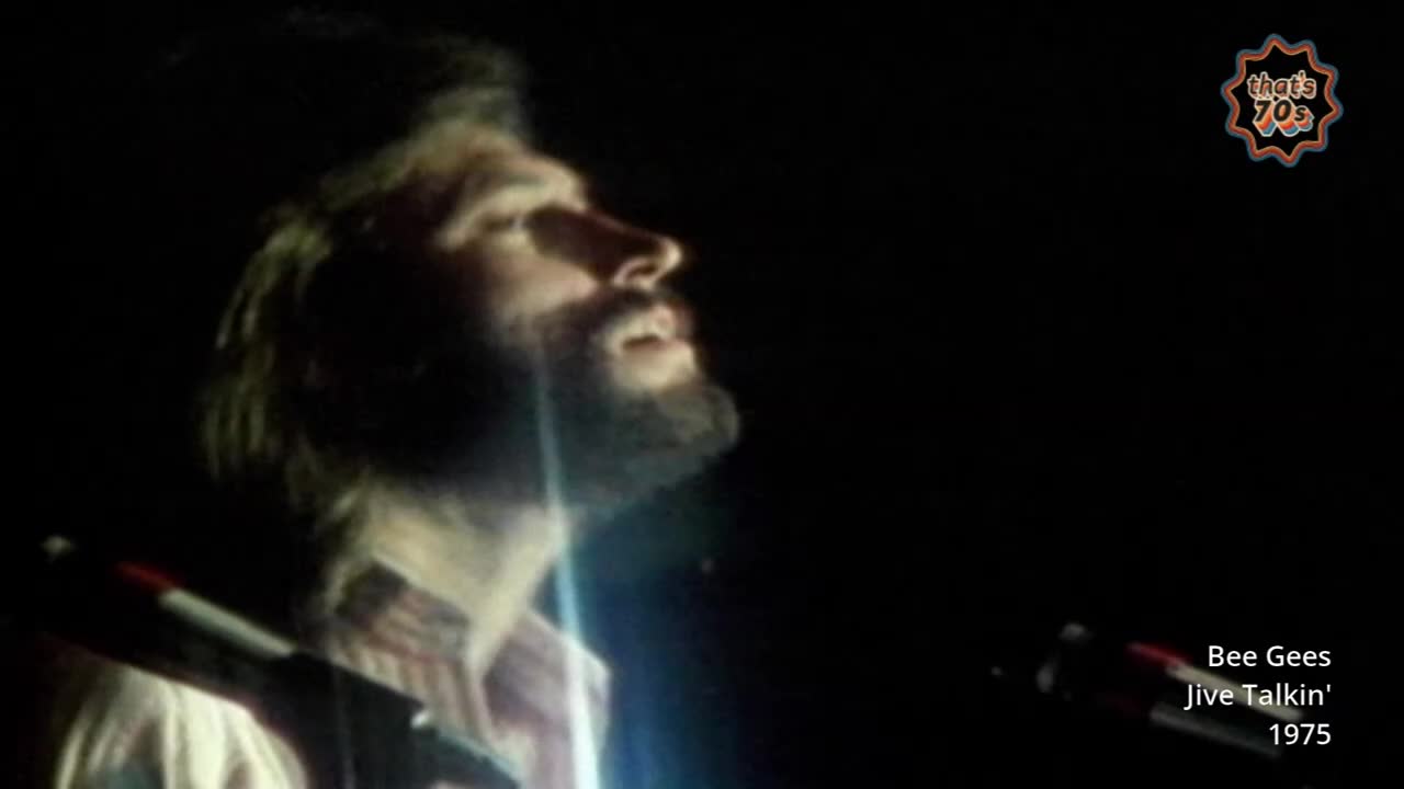 A man with a beard and long hair is singing into a microphone, his head tilted back. The stage lights catch his face as he performs.