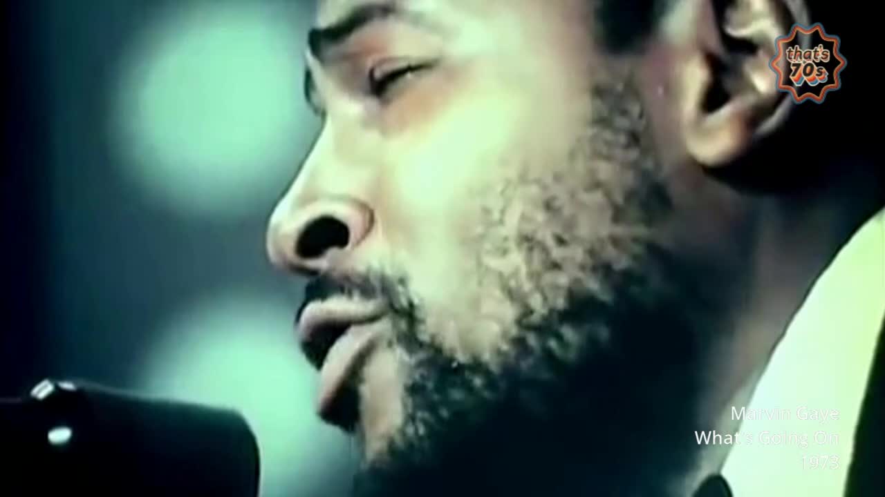 A man's face, close up, with his eyes closed and a beard. He's leaning into a microphone, his lips slightly parted.