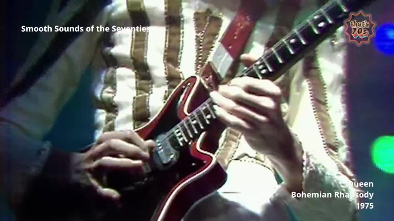 A guitarist's hands move across the fretboard of a red electric guitar. The musician wears a distinctive striped shirt, typical of 1970s British stage wear.