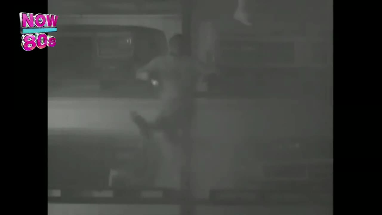 A person is mid-stride, their right leg raised high. The grainy black and white image suggests a scene from the United Kingdom, likely from the Now 80s era.
