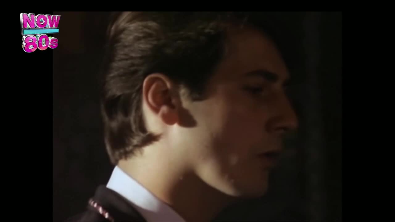 The man's head is turned slightly, his profile illuminated against a dark background. He seems to be speaking, his lips parted, as if delivering a line.
