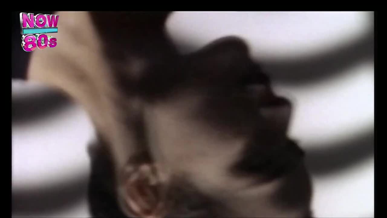 A face, partially obscured, is angled upwards against a bright background. It's a clip from a music video on Now 80s, a channel from the United Kingdom.
