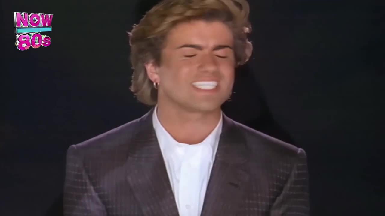 The singer, dressed in a dark suit, is belting out a tune, his eyes closed and mouth open. A "Now 80s" logo sits in the corner, a reminder of the era.
