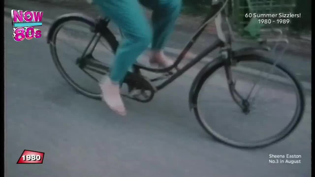 Someone's pedaling a bicycle down the road, their bare feet visible as they push the pedals. The bike's front wheel is turning, and the scene has a vintage feel.
