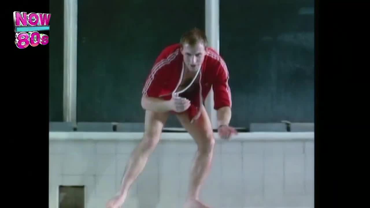 A man in a red tracksuit is skating, his bare feet gliding across a slick surface. He's leaning low, arms outstretched, as if trying to maintain his balance.
