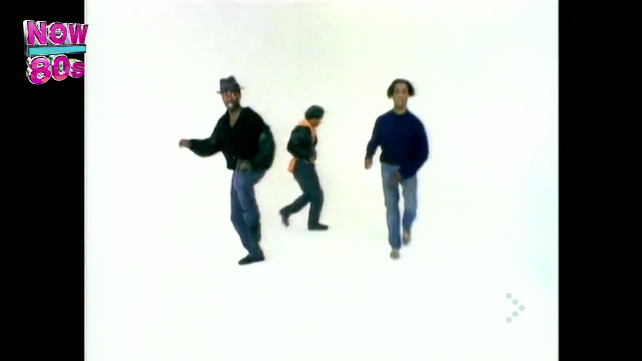 Three men are moving across a stark white background, the one in the middle wearing a bright orange vest. The man on the left is wearing a hat and black jacket, and the one on the right is in a blue sweater.
