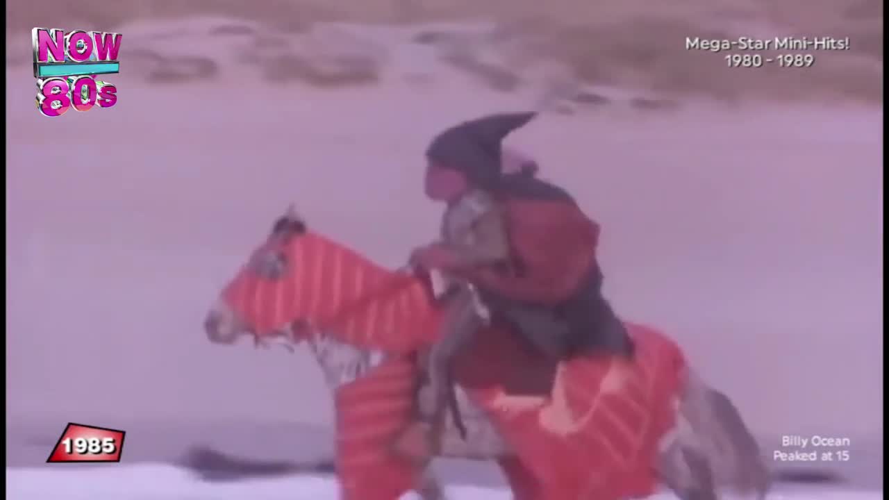 A person in a pointy hat rides a horse, both covered in red fabric, across a pale landscape. The scene is from a music video, probably on Now 80s, and it's a bit silly, but the horse is moving.
