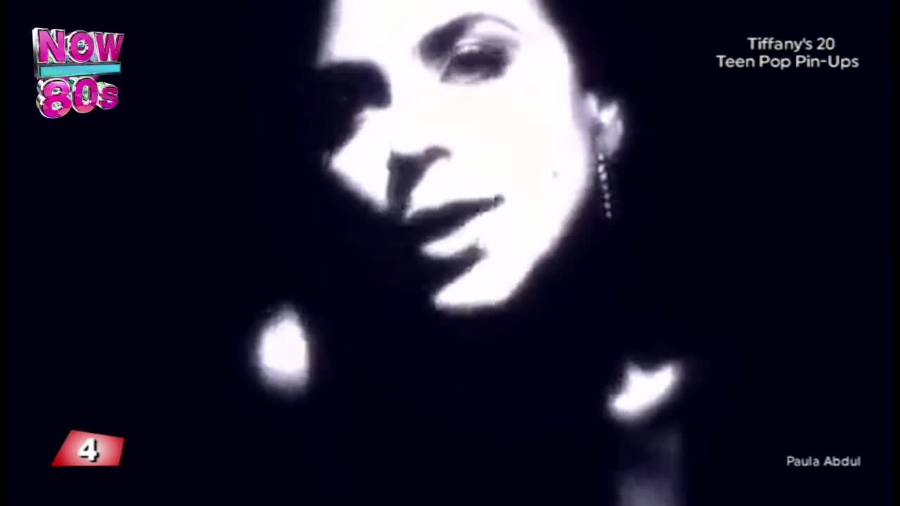 The image is a close-up of a woman's face, her features illuminated against a dark background.  It's a clip from "Tiffany's 20 Teen Pop Pin-Ups" on Now 80s, with Paula Abdul's name visible.
