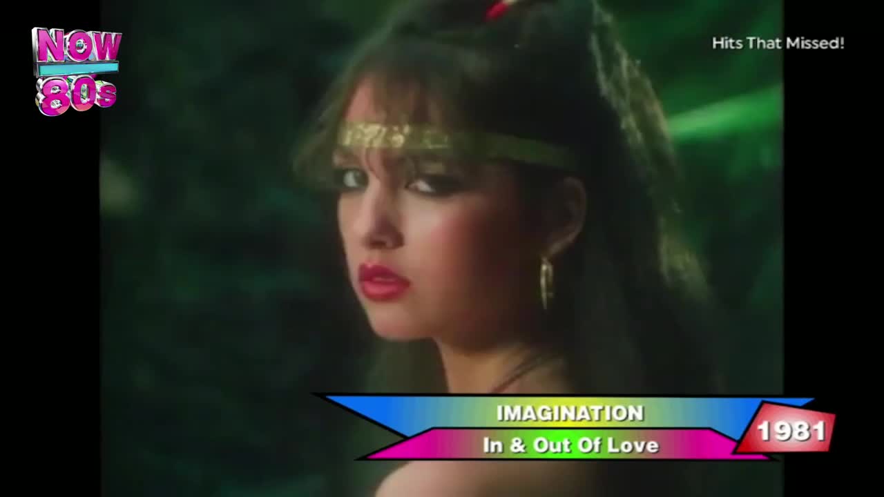 A woman with dark hair and a gold headband looks over her shoulder, her red lips slightly parted. The screen displays the Now 80s logo, and a graphic identifies the song "In & Out Of Love" by Imagination.
