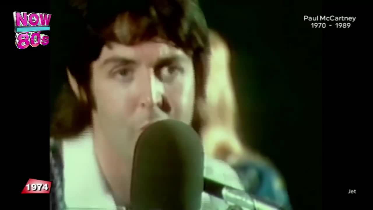 Paul McCartney's face is close to a microphone, his mouth open as if he's singing. Behind him, a woman's blonde hair is visible, and the Now 80s logo sits in the corner.
