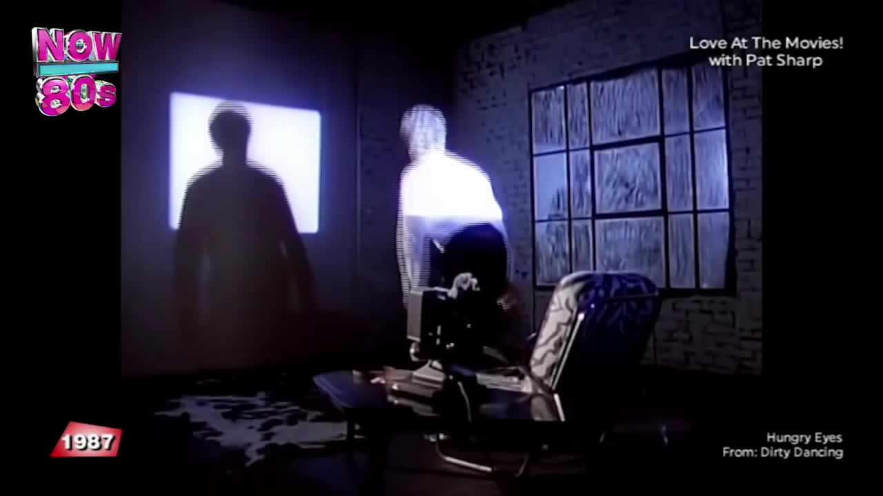 A figure, bleached by the light, stands near a screen displaying a dark silhouette. The scene is dimly lit, with a window's grid reflected on the brick wall.
