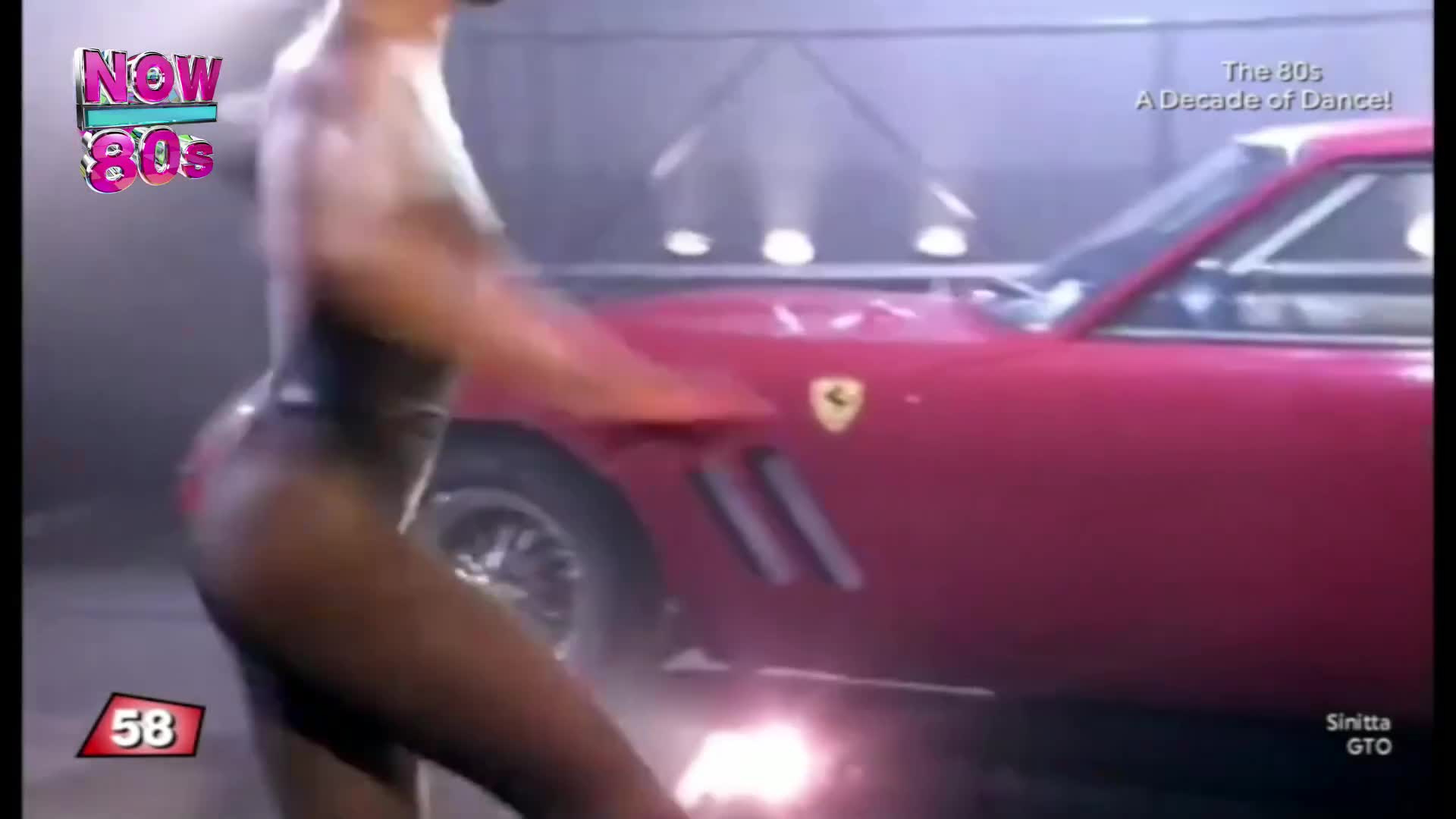 A figure in a leotard is dancing, their arm extended towards a bright red Ferrari. The car's sleek lines and the dancer's movement create a dynamic contrast.
