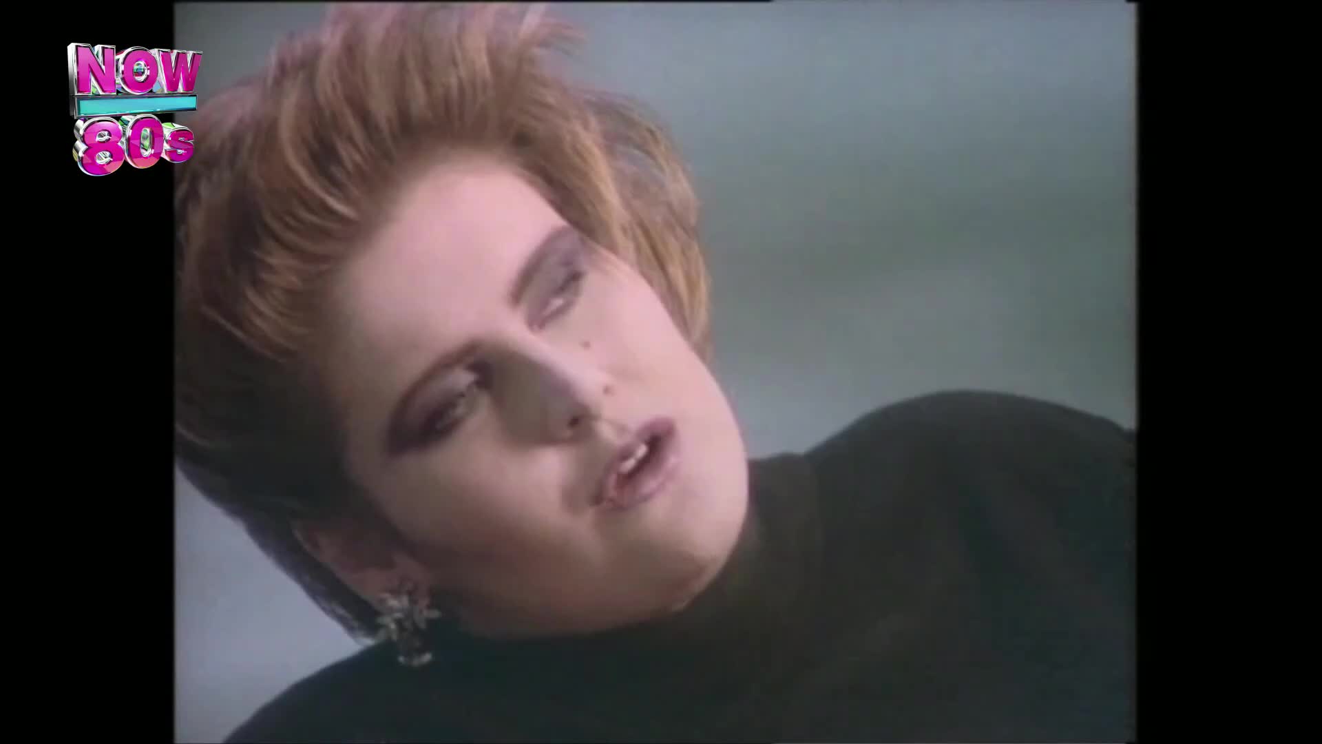 The woman's head is tilted back, her eyes half-closed. She's wearing a black top and a single, ornate earring.
