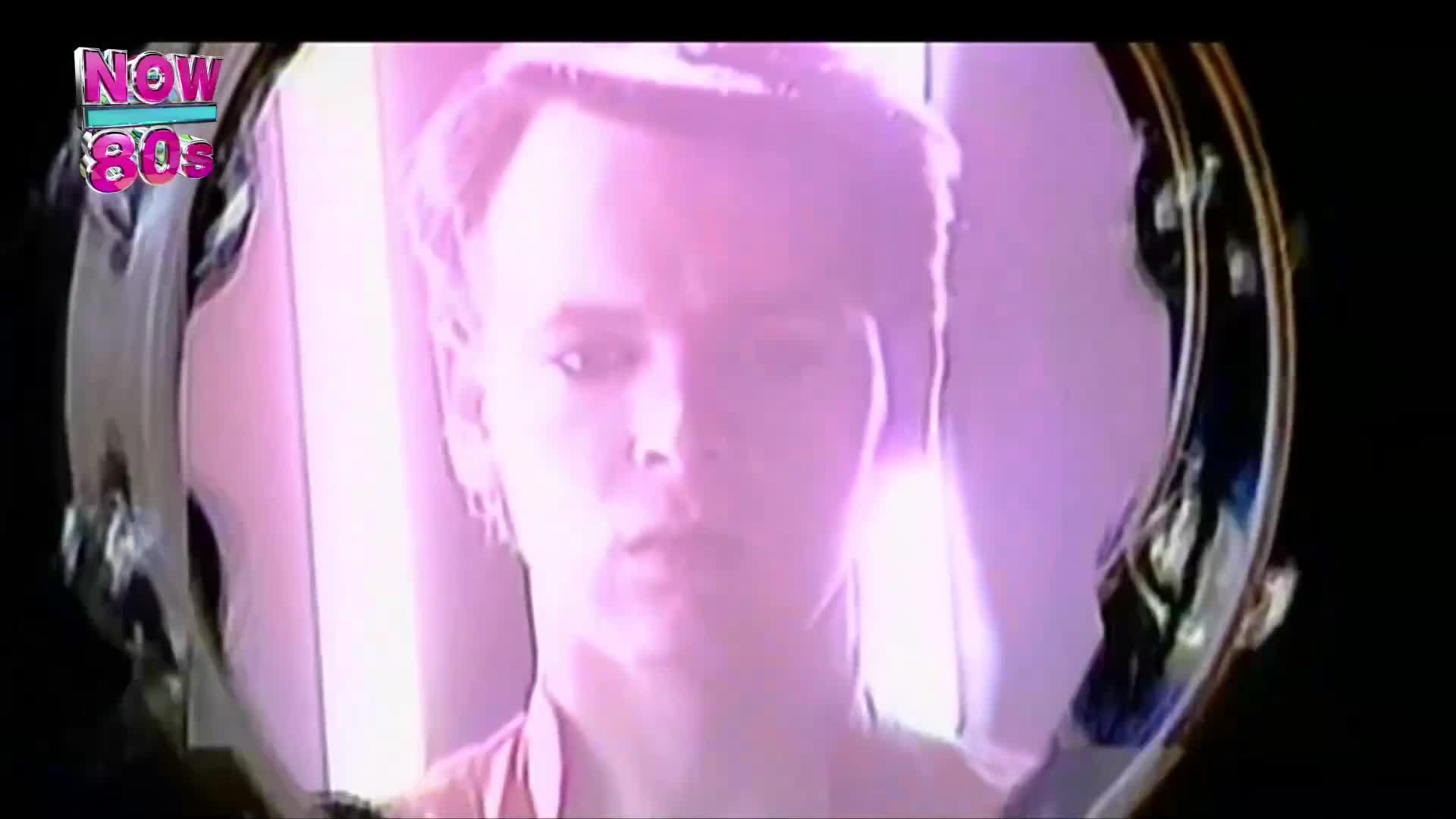 A man's face is reflected in a round mirror, bathed in a soft, pinkish light. The "Now 80s" logo sits in the corner, a reminder of the era's aesthetic.
