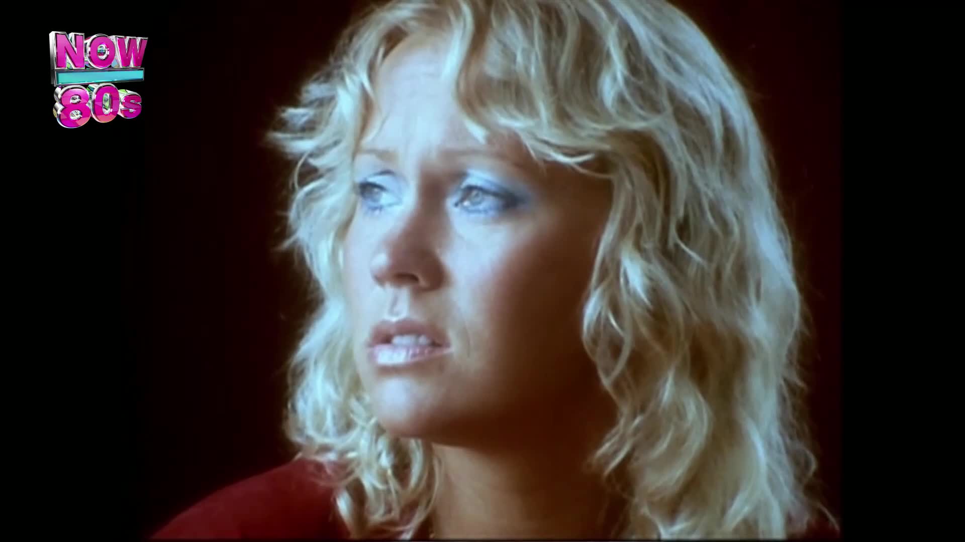 A woman with blonde, wavy hair gazes off-screen, her eyes rimmed with blue shadow. The Now 80s logo sits in the corner, a reminder of the music videos on the telly.
