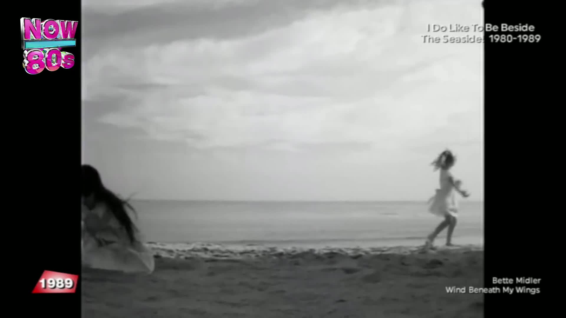 A girl in a light dress runs along the beach, her arms outstretched. Another figure, also in a dress, is crouched near the water's edge.