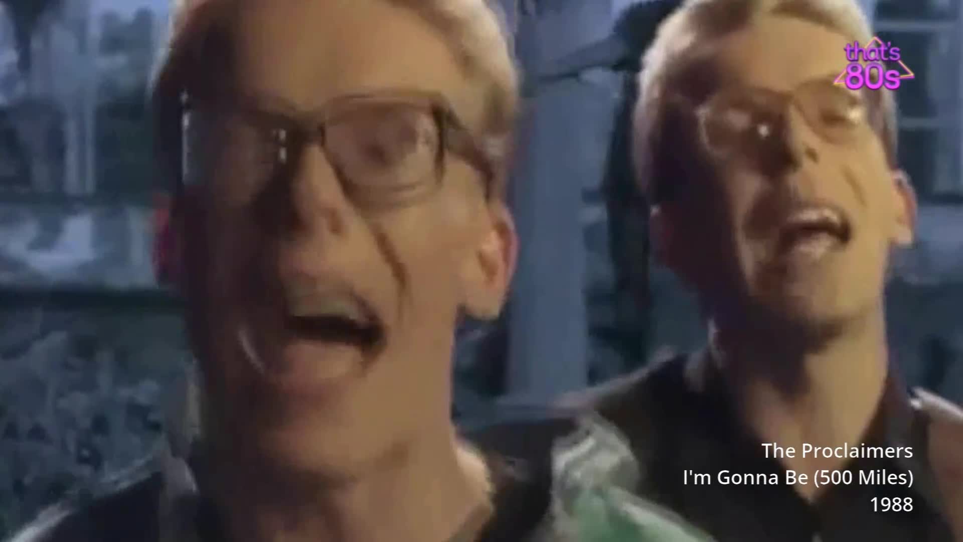 Two men in glasses are singing with their mouths open, their faces close to the camera. The one on the left is in sharp focus, while the other, slightly behind, is softer. Two men in glasses are singing with their mouths open, their faces close to the camera. The one on the left is in sharp focus, while the other, slightly behind, is softer.