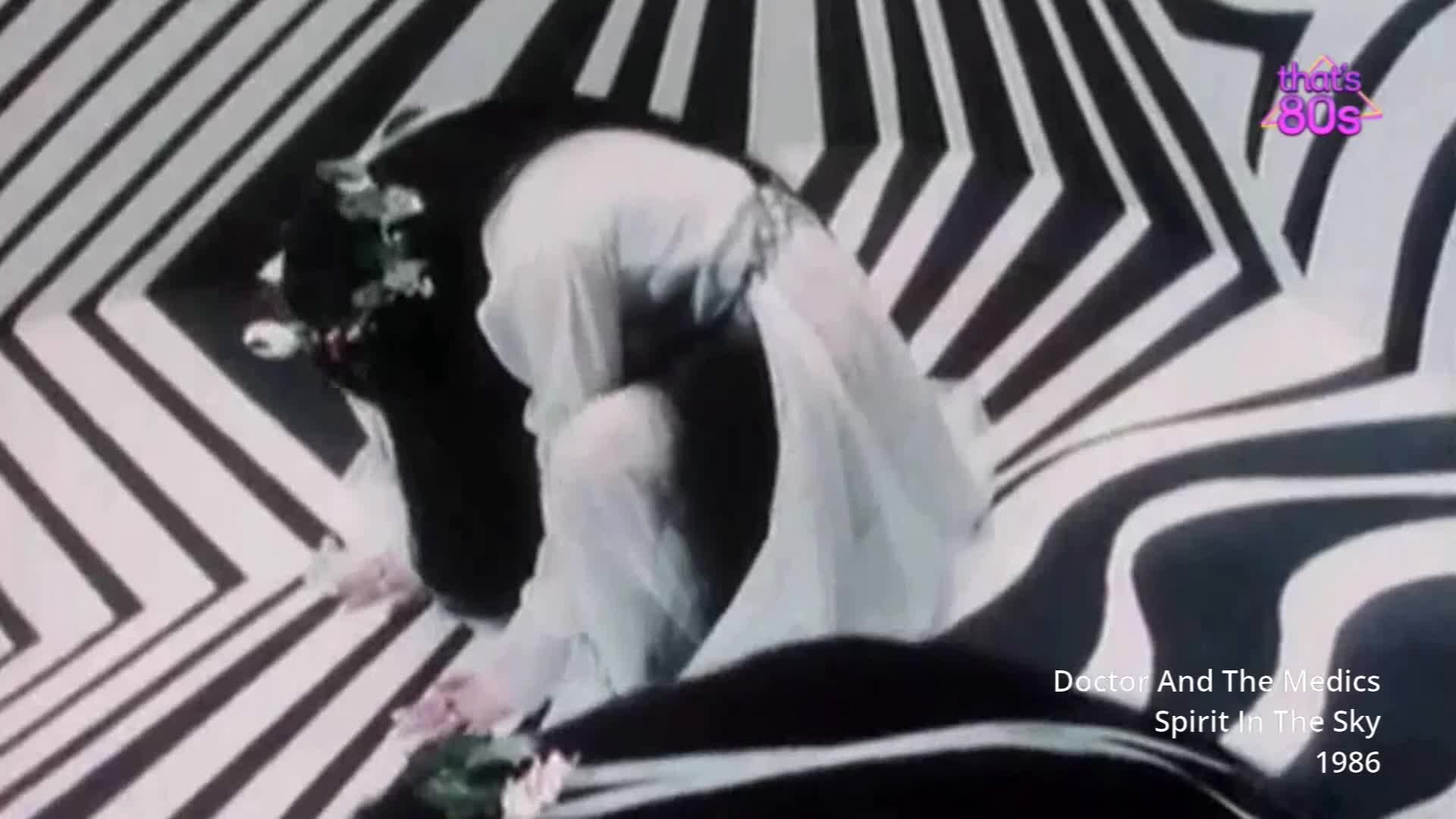 A figure in a flowing white gown kneels, head bowed, amidst a dizzying black and white striped backdrop. Delicate pink flowers are scattered around the figure's hands.